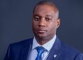 NELSON LUCAS - The Brief | Namibia's Leading Business & Financial News Professional portrait of a man in a navy suit and blue tie against a dark backdrop, presenting a corporate headshot appearance.
