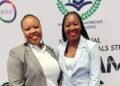 WhatsApp Image 2026-04-16 at 82156 AM - The Brief | Namibia's Leading Business & Financial News Two professional women in blazer suits smile for the camera at a conference backdrop with sponsor logos, including Antal and others.