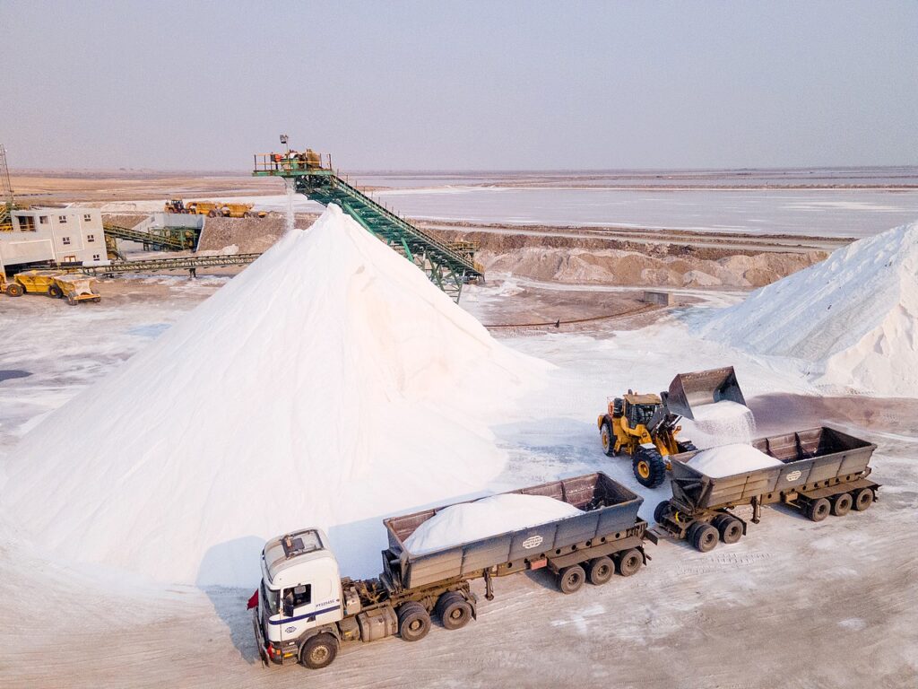 SALT - The Brief | Namibia's Leading Business & Financial News Open-pit salt mine with large white salt piles and trucks unloading salt from dump trucks onto a conveyor system.