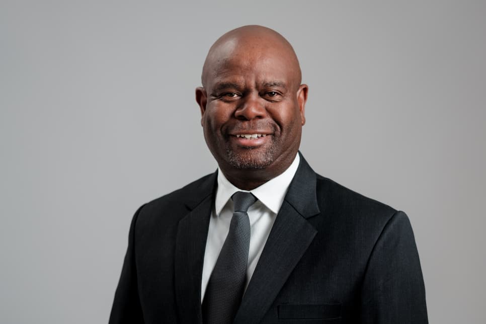Albertus Aochamub1 - The Brief | Namibia's Leading Business & Financial News Smiling man in a dark suit and tie against a gray studio backdrop, looking at the camera, professional headshot.