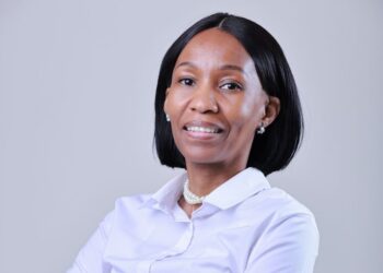 Professional headshot of a smiling woman with short black hair, wearing a white blouse and pearl necklace against a neutral background.