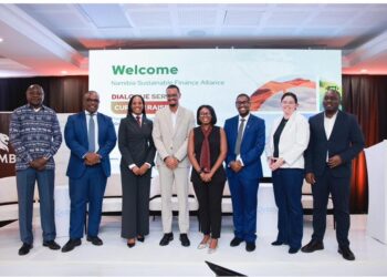 Eight professionals in business attire stand on a stage in front of a screen that reads 'Welcome Namibia Sustainable Finance Alliance'.