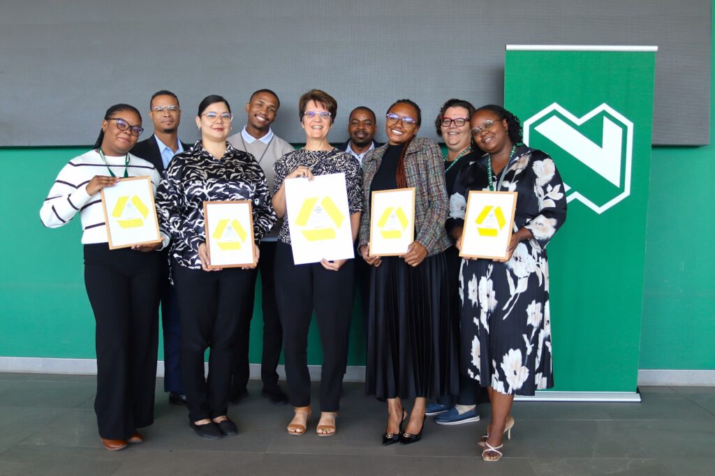 WhatsApp Image 2026-04-21 at 112902 AM - The Brief | Namibia's Leading Business & Financial News Group of eight professionals posing with framed certificates at a ceremony, in front of a green wall with a logo behind them.