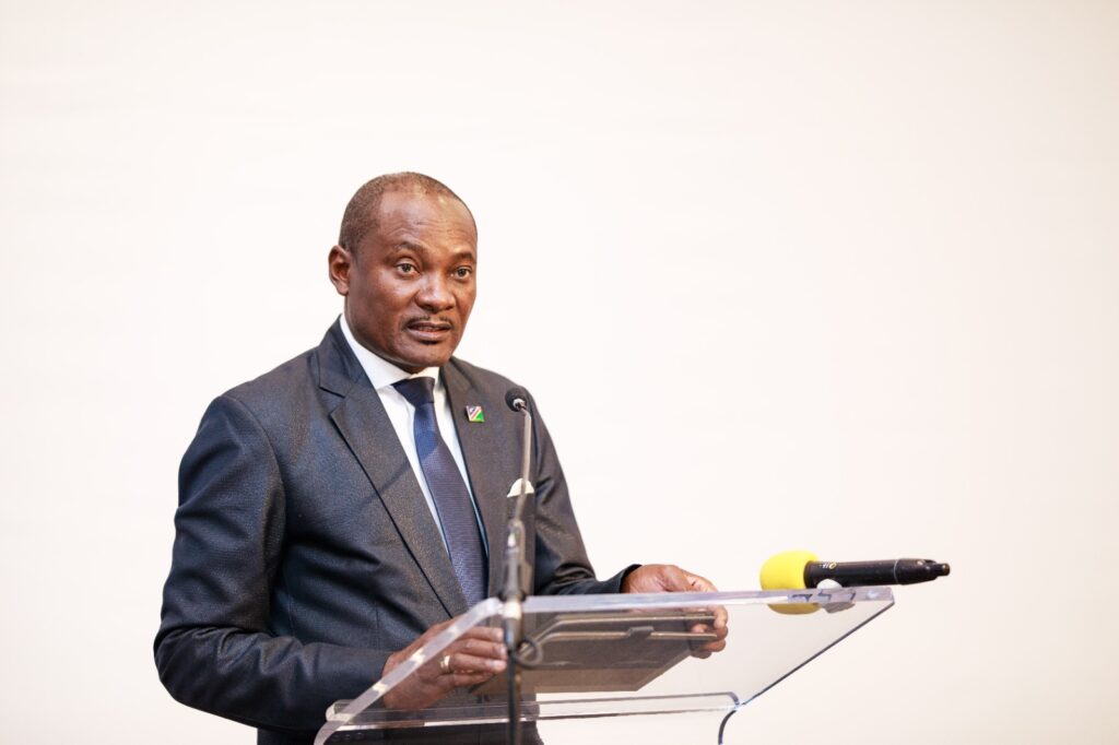 Man in a dark suit and blue tie delivering a speech at a clear lectern with microphones.