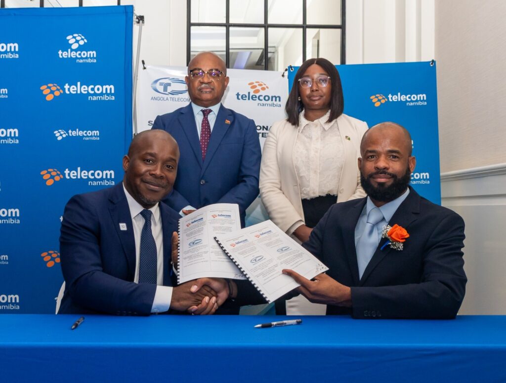 Four people in business attire pose with signed documents at a table, Telecom Namibia banners in blue behind them.