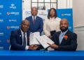 Four people in business attire pose with signed documents at a table, Telecom Namibia banners in blue behind them.