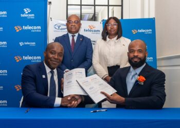 Four people in business attire pose with signed documents at a table, Telecom Namibia banners in blue behind them.