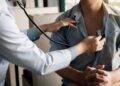 Doctor auscultating a patient with a stethoscope on the chest during a medical exam.