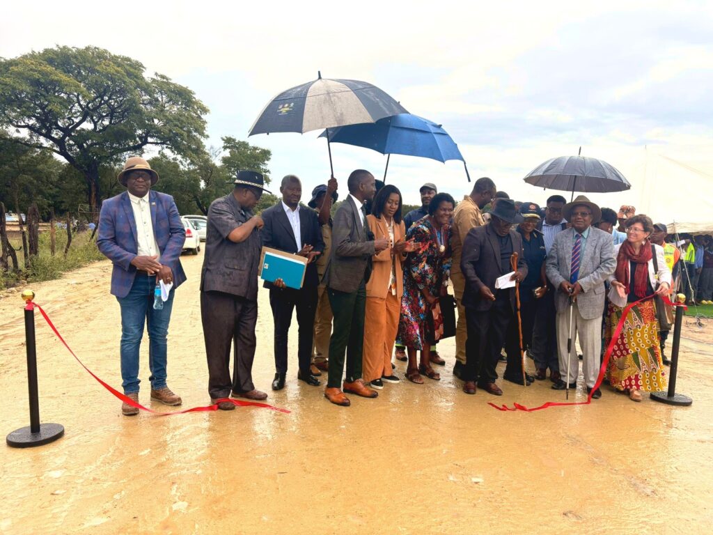 WhatsApp Image 2026-04-29 at 51116 PM - The Brief | Namibia's Leading Business & Financial News Group of formally dressed people at a ribbon-cutting ceremony outdoors, some holding documents and umbrellas in light rain on a muddy path.