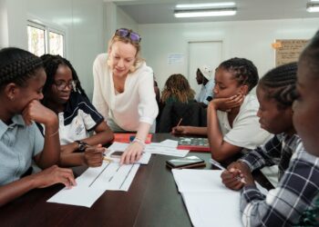 Teacher leaning over a table to help diverse students with worksheets in a bright classroom.