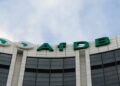 Exterior view of a modern bank building with green letters reading 'AfDB' along a curved white facade. Two circular logos with Africa map to the left.