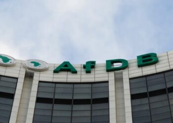 Exterior view of a modern bank building with green letters reading 'AfDB' along a curved white facade. Two circular logos with Africa map to the left.