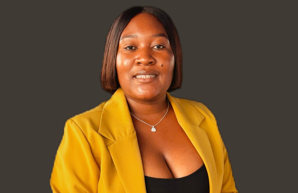 Portrait of a woman wearing a yellow blazer against a dark background, looking at the camera.