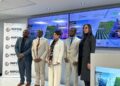 Five professionals in business attire stand in front of screens and a NIPDB banner at a conference event.