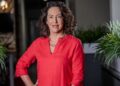 Capricorn Elize Smith 2 1 1 1 - The Brief | Namibia's Leading Business & Financial News Portrait of a smiling woman with curly dark hair wearing a red blouse, standing between potted plants in an office-like setting.