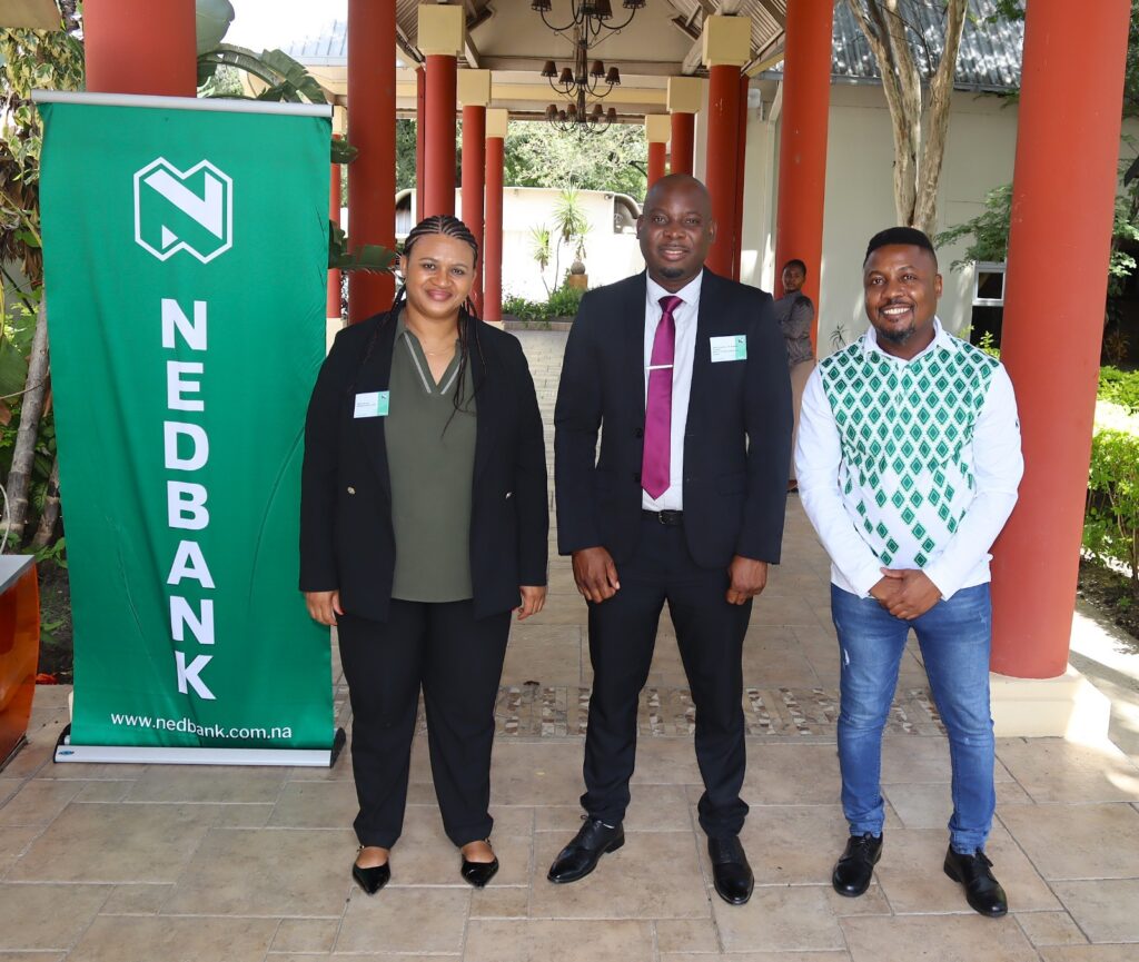 WhatsApp Image 2026-05-07 at 74924 AM - The Brief | Namibia's Leading Business & Financial News Three people pose for a group photo beside a green Nedbank banner outdoors.