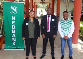 Three people pose for a group photo beside a green Nedbank banner outdoors.