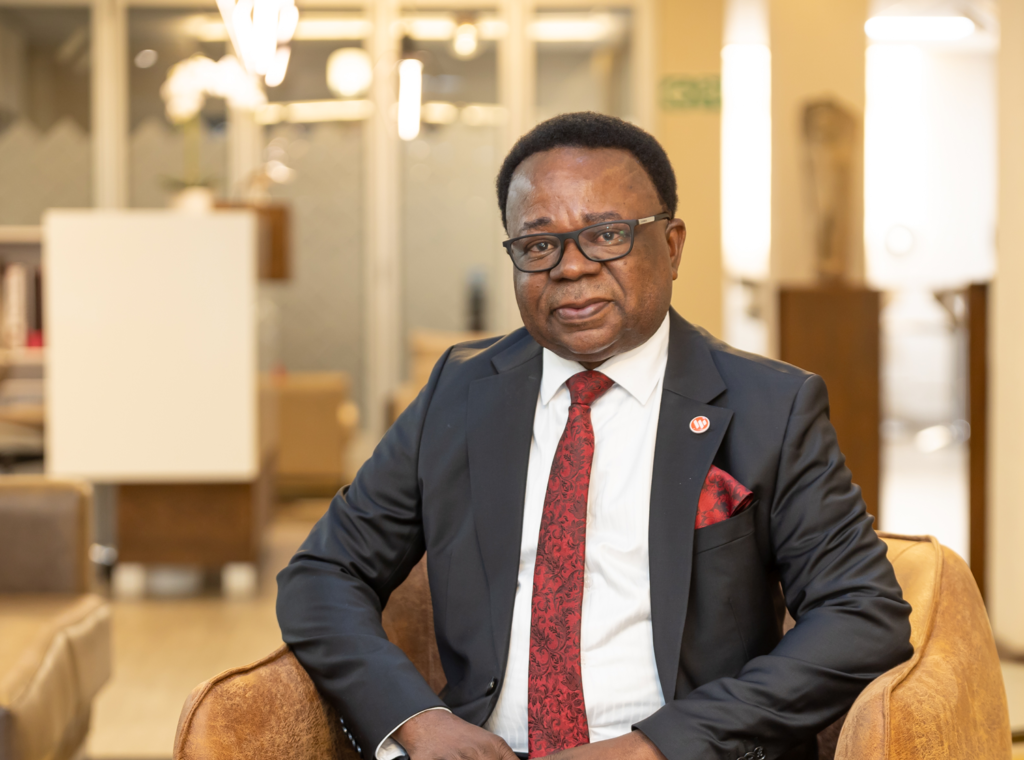 David-Nuyoma-2025-Media - The Brief | Namibia's Leading Business & Financial News Professional portrait of a man in a dark suit and red tie sitting in a beige chair in a modern office lounge.