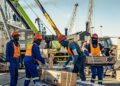 ERONGO MARINE - The Brief | Namibia's Leading Business & Financial News Group of workers in orange safety vests and hard hats handling cardboard boxes at a busy dock, with cranes and stacked pallets in the background.
