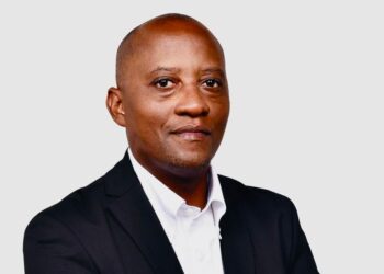 Professional headshot of a man in a black suit and white shirt against a light gray background, facing the camera.