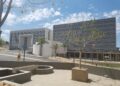 CITY OF WINDHOEK - The Brief | Namibia's Leading Business & Financial News White contemporary building with large metal louvers, palm trees, and a paved plaza under a blue sky with scattered clouds in the foreground.