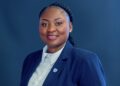 Hellen Amupolo - The Brief | Namibia's Leading Business & Financial News Professional headshot of a smiling woman in a navy blazer and white shirt against a blue background with a small lapel pin