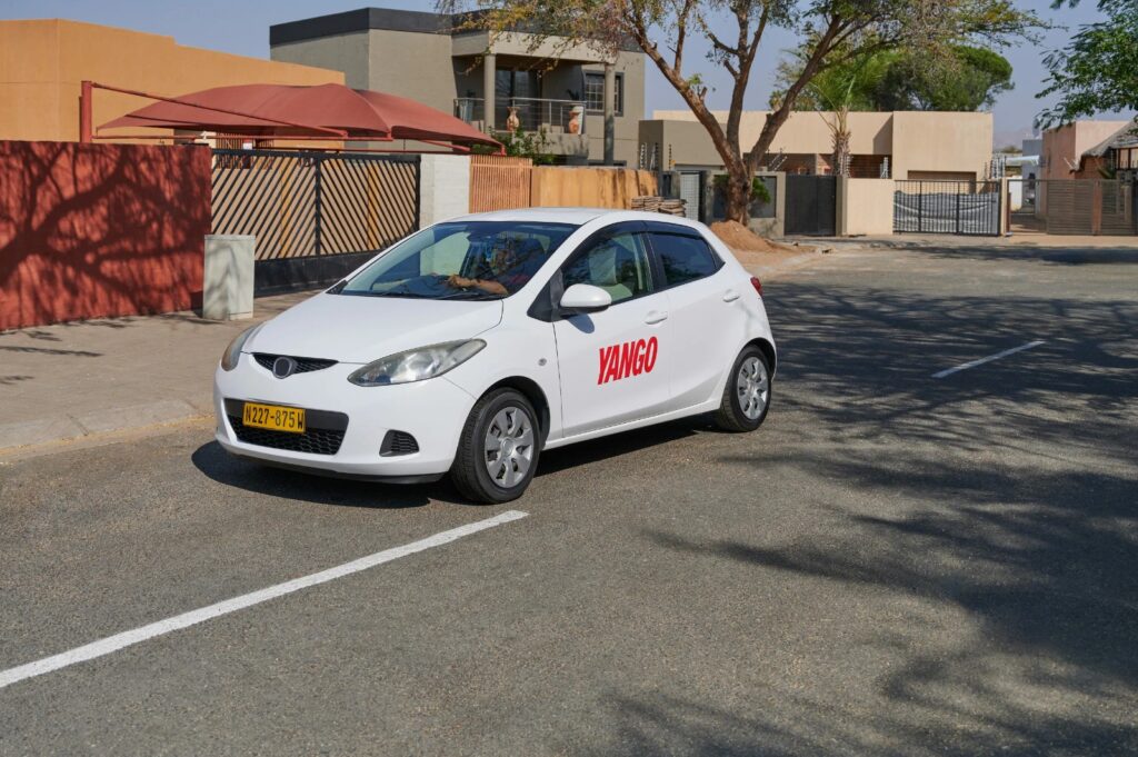 White sedan with 'YANGO' branding parked on a residential street, front wheel turned slightly left.