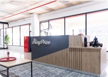 Open-office reception desk labeled 'KingPrice' in a bright glass-walled lobby, with a round table and a small action figure in the foreground.