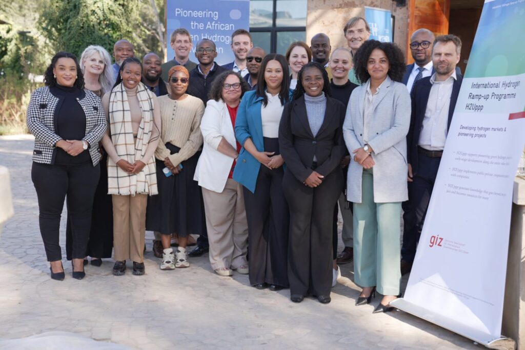 Diverse group of professionals posing outdoors at a conference, with hydrogen program banners in the background.