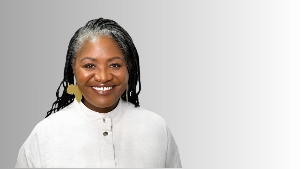 Margaret Gustavo 1 - The Brief | Namibia's Leading Business & Financial News Smiling African American woman with braided hair and gold earrings, wearing a light gray buttoned top, against a gray gradient background.