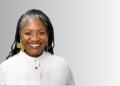 Margaret Gustavo 1 - The Brief | Namibia's Leading Business & Financial News Smiling African American woman with braided hair and gold earrings, wearing a light gray buttoned top, against a gray gradient background.