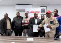 Group of men in an office posing with signed documents in front of a MEATCO banner and framed photos, indicating a formal agreement ceremony.