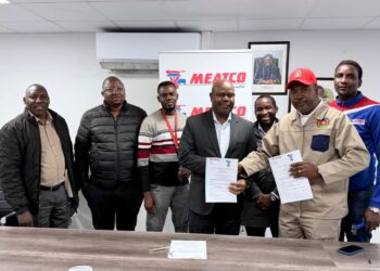 Group of men in an office posing with signed documents in front of a MEATCO banner and framed photos, indicating a formal agreement ceremony.