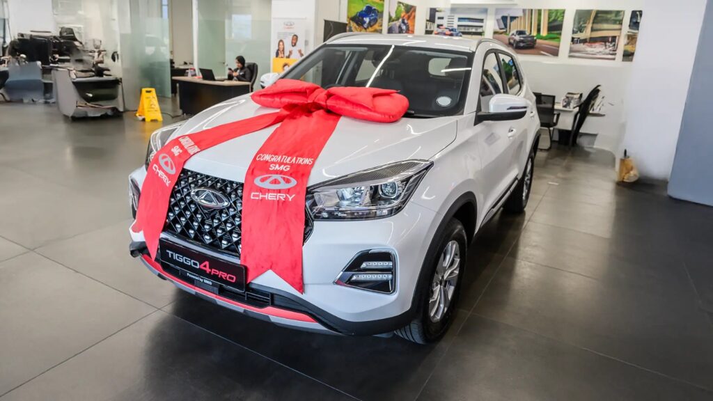 Tiggo4pro - The Brief | Namibia's Leading Business & Financial News New white Chery Tiggo 4 Pro SUV in a showroom, wrapped with a large red bow and ribbon for a gift celebration.