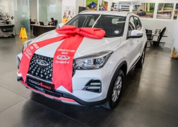 New white Chery Tiggo 4 Pro SUV in a showroom, wrapped with a large red bow and ribbon for a gift celebration.