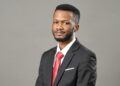 TIO NAKASOLE - The Brief | Namibia's Leading Business & Financial News Portrait of a man in a dark suit and red tie, looking at the camera against a plain gray background, with a white pocket square.