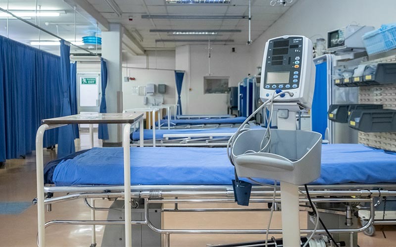 Hospital Bed - The Brief | Namibia's Leading Business & Financial News Hospital ward with blue-sheeted beds, privacy curtains, and a patient monitor in the foreground.