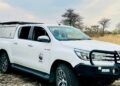 White WWF-branded pickup truck parked on a dry, grassy plain with leafless trees in the distance.