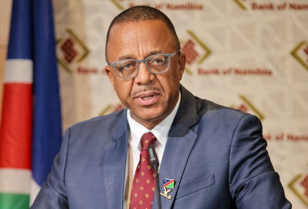 WhatsApp Image 2026-05-21 at 51541 PM - The Brief | Namibia's Leading Business & Financial News Man in a blue suit and red patterned tie speaks into a microphone at a podium, with a Namibian flag and Bank of Namibia backdrop behind him.