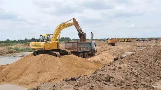 sand mining - The Brief | Namibia's Leading Business & Financial News Yellow excavator loading dirt into a dump truck at a construction site, with a sandy trench and distant equipment on the horizon.