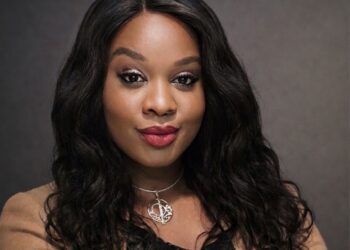 CHISOM - The Brief | Namibia's Leading Business & Financial News Portrait of a woman with long wavy black hair, wearing a beige blazer and a silver pendant necklace, smiling softly against a dark gray backdrop.