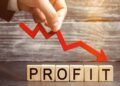 Hand placing a red downwards arrow over wooden cubes spelling PROFIT, symbolizing falling profits.