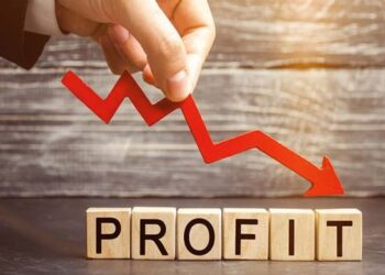Hand placing a red downwards arrow over wooden cubes spelling PROFIT, symbolizing falling profits.