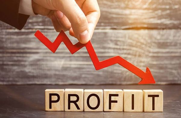 Hand placing a red downwards arrow over wooden cubes spelling PROFIT, symbolizing falling profits.