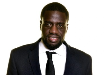 Portrait of a smiling African American man in a dark suit and black tie against a white background, a professional headshot.