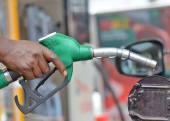 Close-up of a person fueling a car with a green gas pump nozzle at the fuel cap.