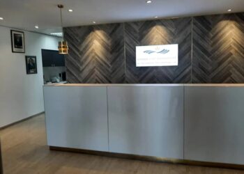 Reception desk in a modern office lobby with a dark chevron wood accent wall and a Namibian Asset Management sign above it