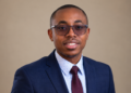 Willem Kanyondi - The Brief | Namibia's Leading Business & Financial News Professional headshot of a man in a navy suit, white dotted shirt, burgundy tie, and glasses, smiling at the camera.