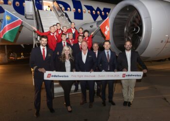 Group of airline staff posing in front of a parked Edelweiss airplane on the tarmac, holding a banner announcing the first flight Windhoek–Zurich on 01.06.2026, with Namibia and Swiss flags visible.