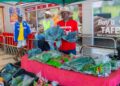 WhatsApp Image 2026-06-02 at 50544 PM - The Brief | Namibia's Leading Business & Financial News Vendor in a red shirt and wide-brim hat sells leafy greens at a market stall inside a store, with bags of vegetables on a red checkered table.
